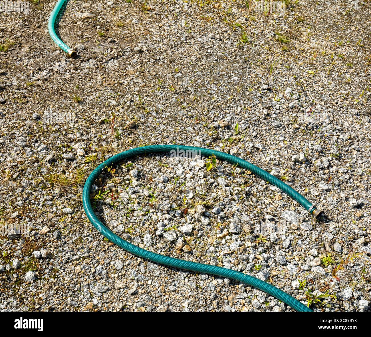 Zwei Enden der abgeklemmten, unterschiedlich farbigen grünen Wasserschläuche, die auf dem Boden liegen Stockfoto