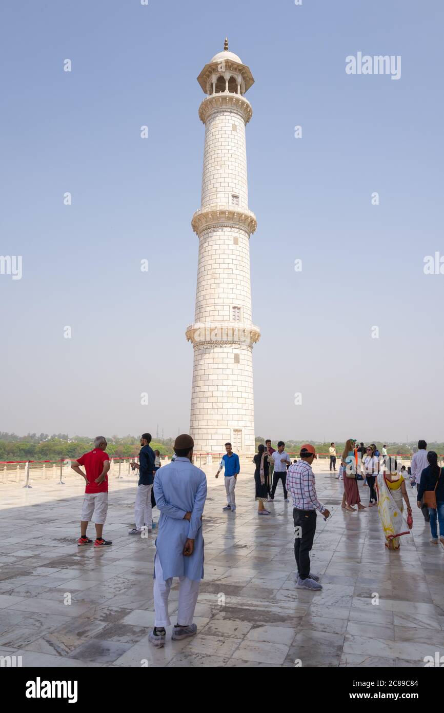 Besucher in traditioneller und westlicher Kleidung an einem sonnigen Tag zum Taj Mahal, das nahe einem der vier Minarette abgebildet wird Stockfoto