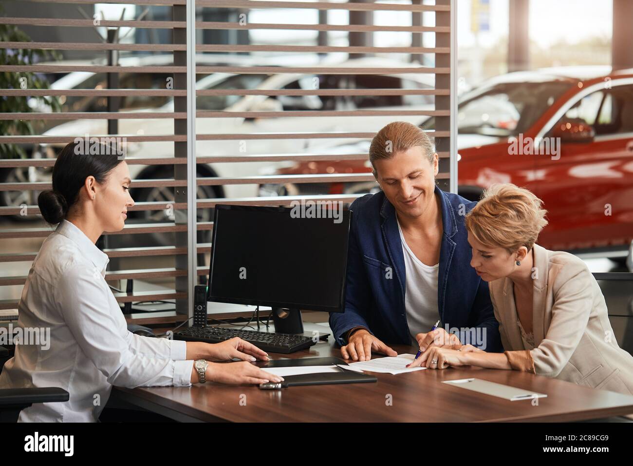 Sales Agent am Tisch Schreibtisch über Auto Funktionen zu fröhlichen paar  Kunden im Autohaus Büro Stockfotografie - Alamy