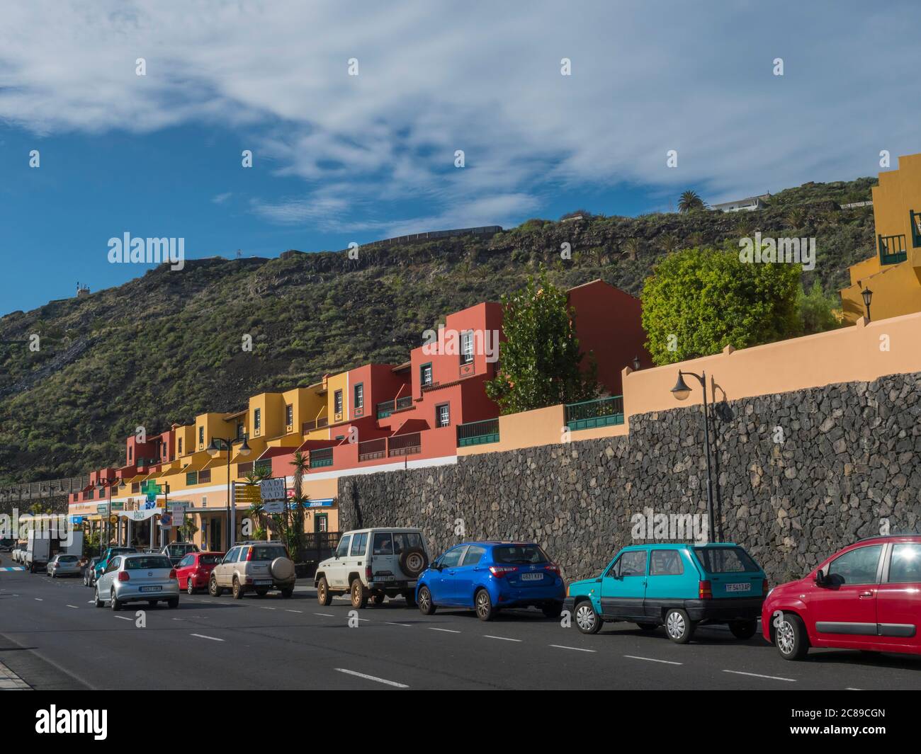 Los Cancajos, La Palma, Kanarische Inseln, Spanien, 22. Dezember 2019: Farbenfrohe gelbe und rote Appartementhäuser und geparktes Auto an der Hauptstraße mit Stockfoto Los Cancajos, La Palma, Kanarische Inseln, Spanien, 22. Dezember 2019: Farbenfrohe gelbe und rote Appartementhäuser und geparktes Auto an der Hauptstraße mit Stockfoto