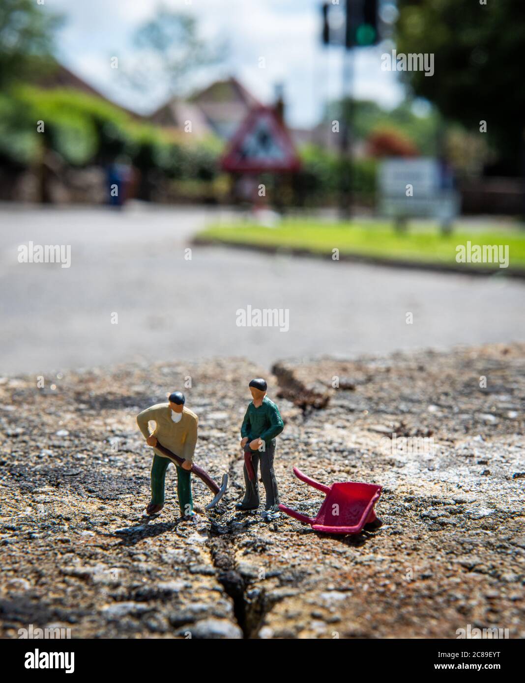 Miniaturmenschen, zwei Arbeiterfiguren, die einen Riss in der Straße in Lennoxtown, Schottland reparieren Stockfoto