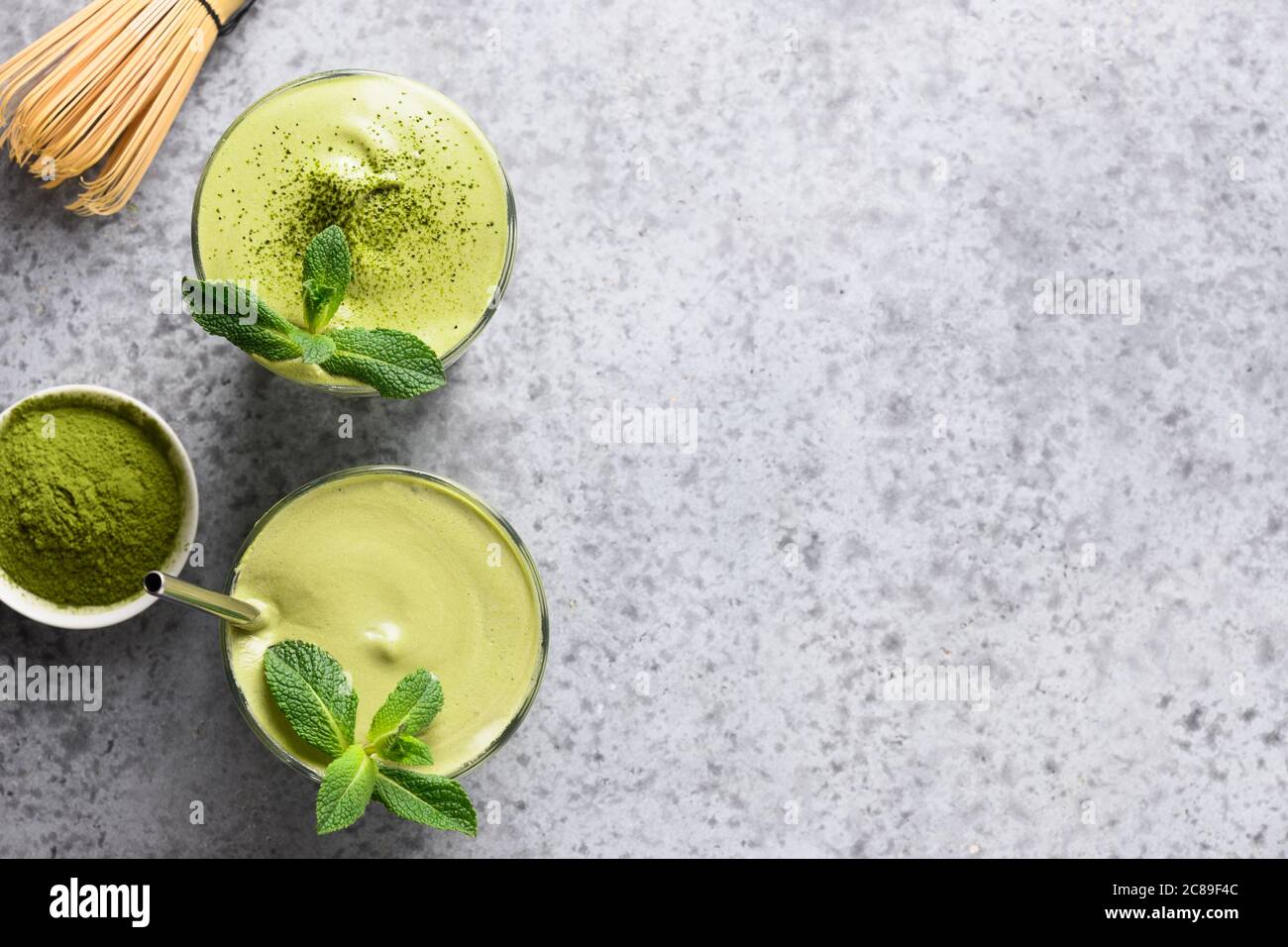 Dalgona Matcha Latte Tee, Bambusbesen und Matcha Pulver auf grau. Stockfoto