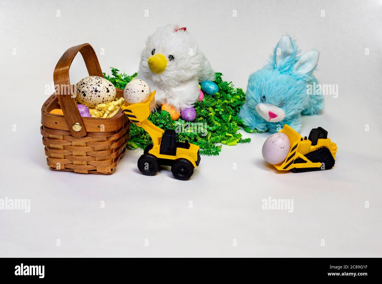 Osterfoto von Stufed Hase und Henne mit verzierten Ostereiern, einem Korb und einem Kinderspielzeug-Bauwagen. Stockfoto