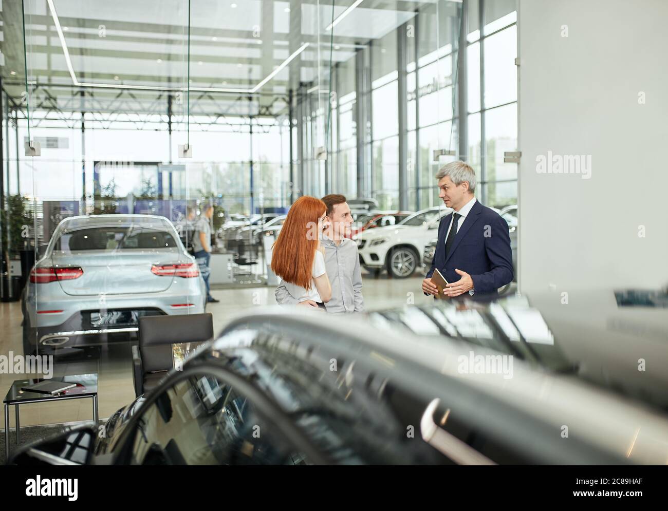 Sales Agent am Tisch Schreibtisch über Auto Funktionen zu fröhlichen paar  Kunden im Autohaus Büro Stockfotografie - Alamy