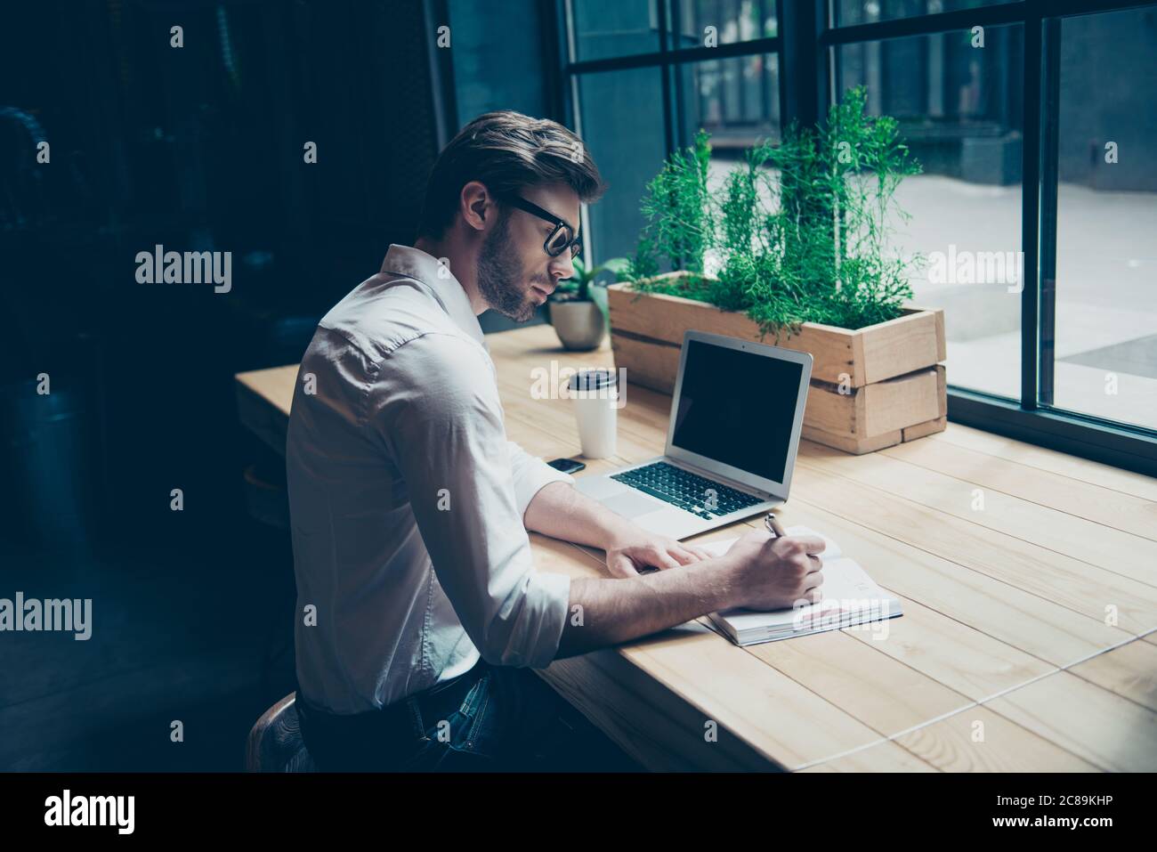 Rückansicht eines Journalisten stilvoller Typ, der in einem Arbeitsraum in Coworking im Loft-Stil, gut gekleidet, in einer Brille eine Geschichte schreibt Stockfoto