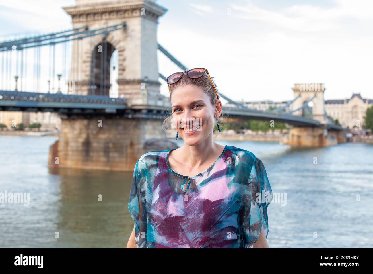 Glückliche junge positive Frau mit toothy Lächeln posiert in Chain Bridge, Budapest, Ungarn Stockfoto