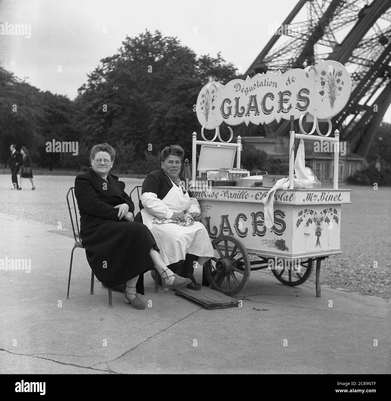 1950er Jahre, historisch, Paris, Frankreich, am Champ de Mars beim Eiffelturm an einem kleinen mobilen Eiswagen, eine Dame, die die Stadt besucht, die neben der Kauffrau Madame Binet sitzt. Stockfoto
