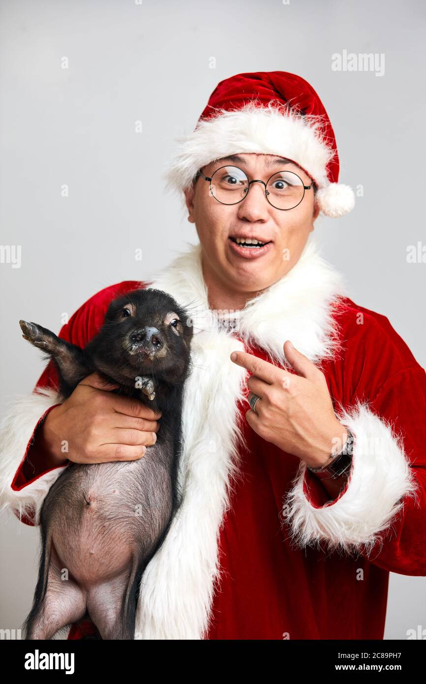 Asiatischer Weihnachtsmann in Weihnachtsanzug zeigt auf kleine schwarze  Piggy, Blick auf Kamera mit Frage Gesichtsausdruck, isoliert über weiß  Stockfotografie - Alamy
