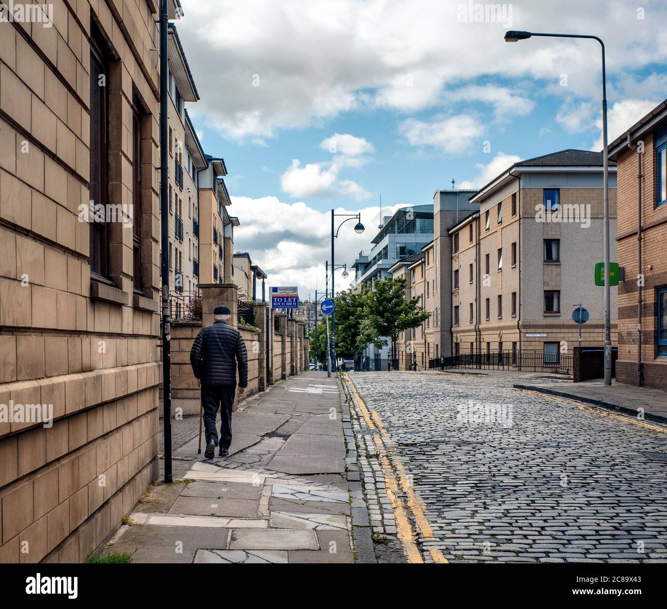 Ein älterer Mann mit einem Spazierstock geht entlang High Riggs, Fountainbridge, Edinburgh, Schottland, Großbritannien. Stockfoto