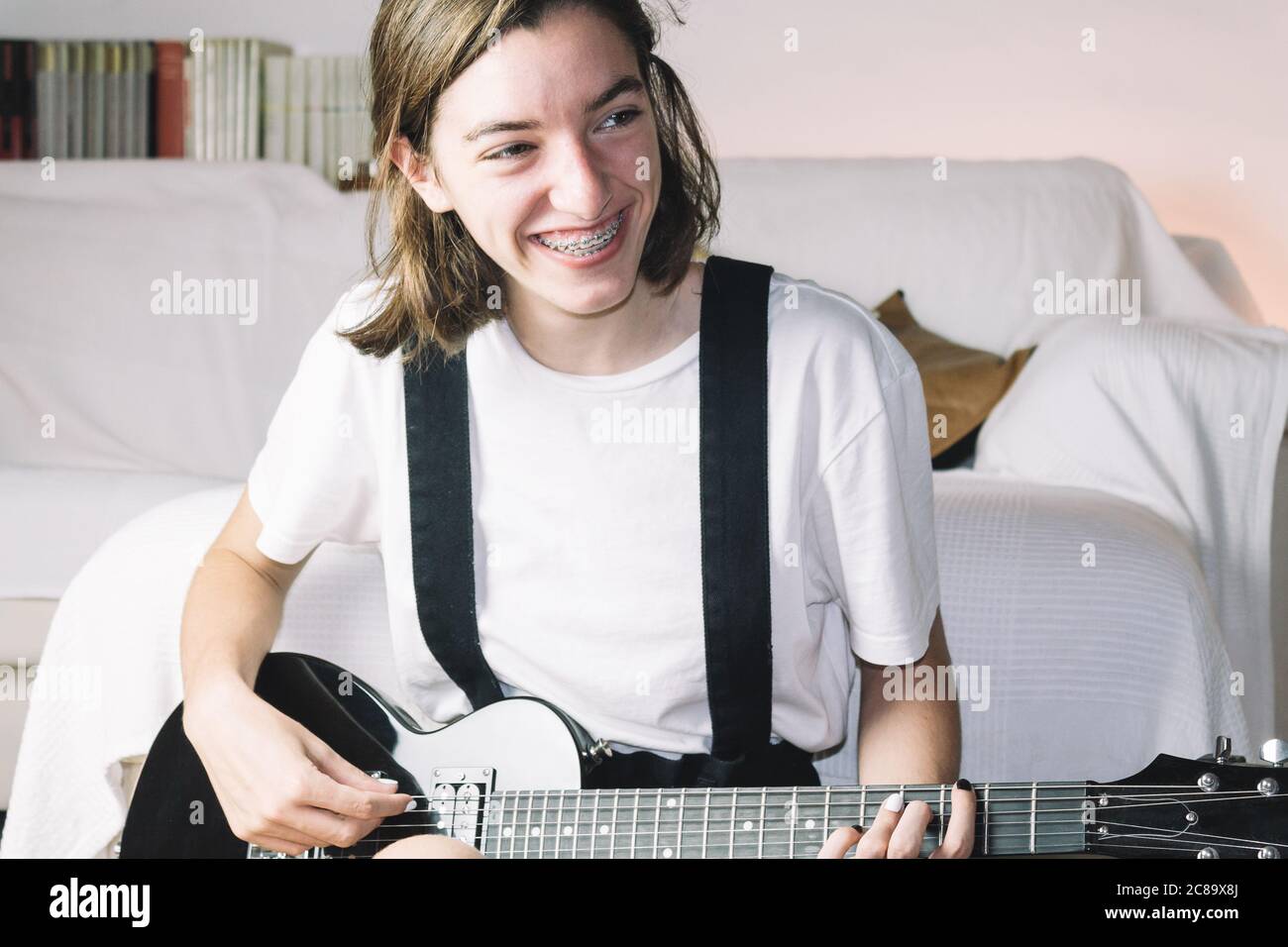 Ein Teenage-Mädchen in Zahnspangen, das mit einem Lächeln Gitarre spielt. Konzept des Lächelns beim Lernen. Stockfoto