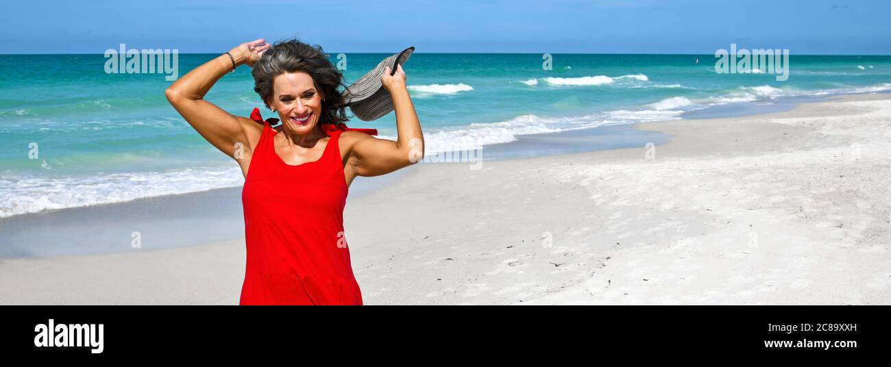 Schöne Reife Frau, Die Ein rotes Sommerkleid am Strand trägt Stockfoto