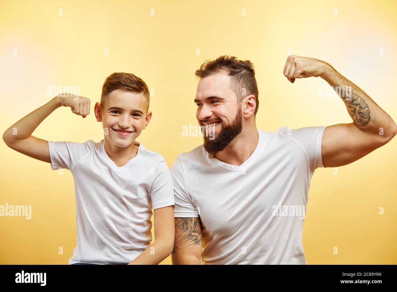 Schöner bärtiger Vater und sein Sohn schauen auf Kamera und lächeln, während Bizeps zeigen Stockfoto