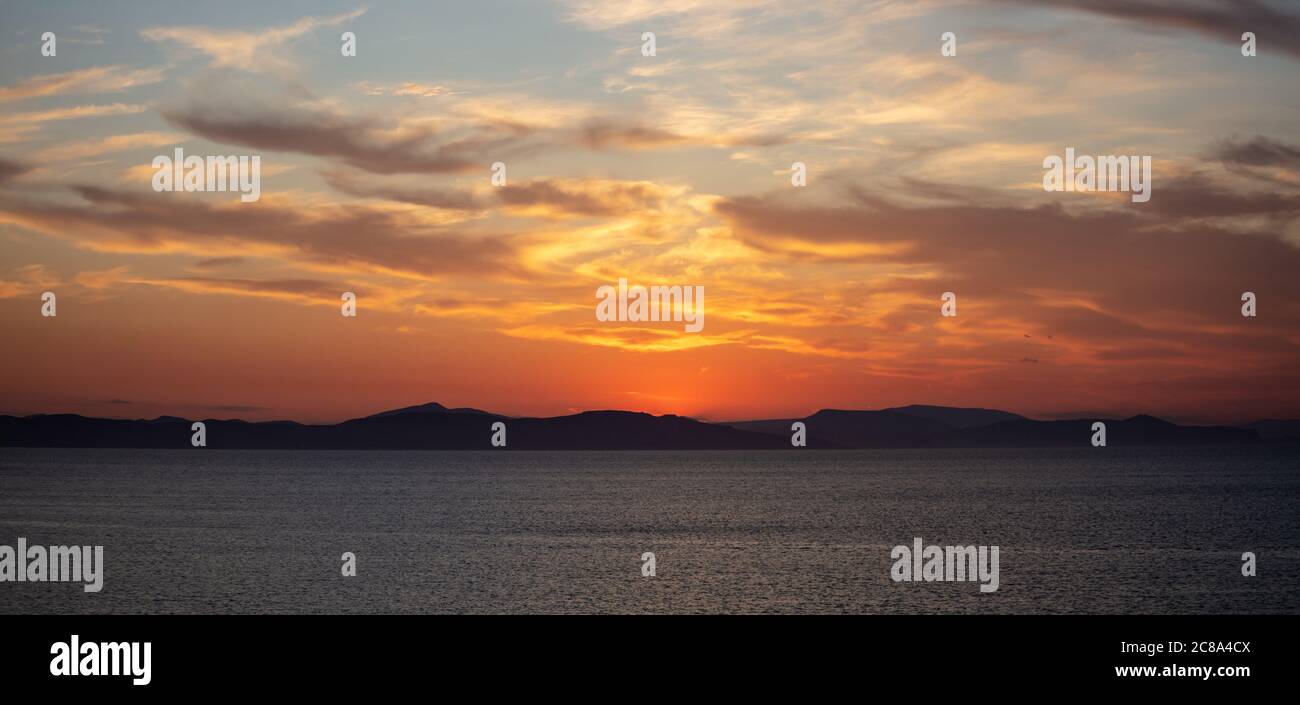 Sonnenuntergang orange Wolkenlandschaft über dem Meerwasser. Dramatische magische Sonnenaufgangslandschaft in Ägäis Griechenland. Dämmerung, Dämmerung Hintergrund. Dunkles Inselland und Orang Stockfoto