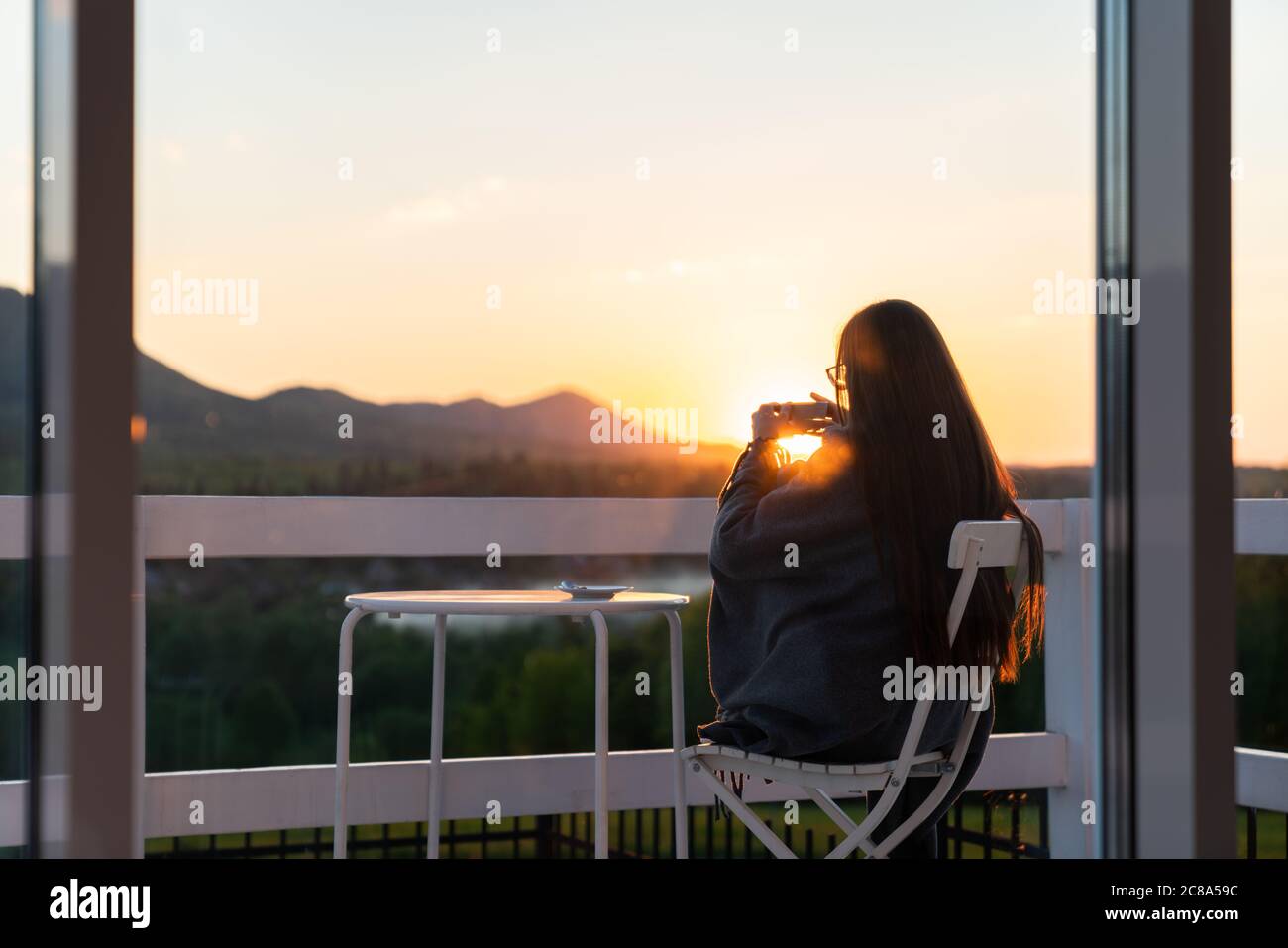 Junge schöne Frau genießt den Tee mit Kräutern auf der Terrasse eines Cafés in den Bergen auf einem Sonnenset Stockfoto