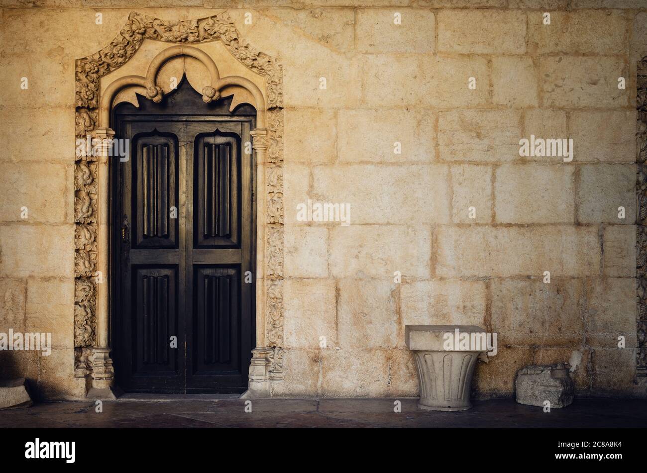 Alte Holztür durch die gelbe Steinmauer des Kreuzgangs eines antiken portugiesischen Klosters mit traditionellen manuelinischen spätgotischen Mustern Stockfoto