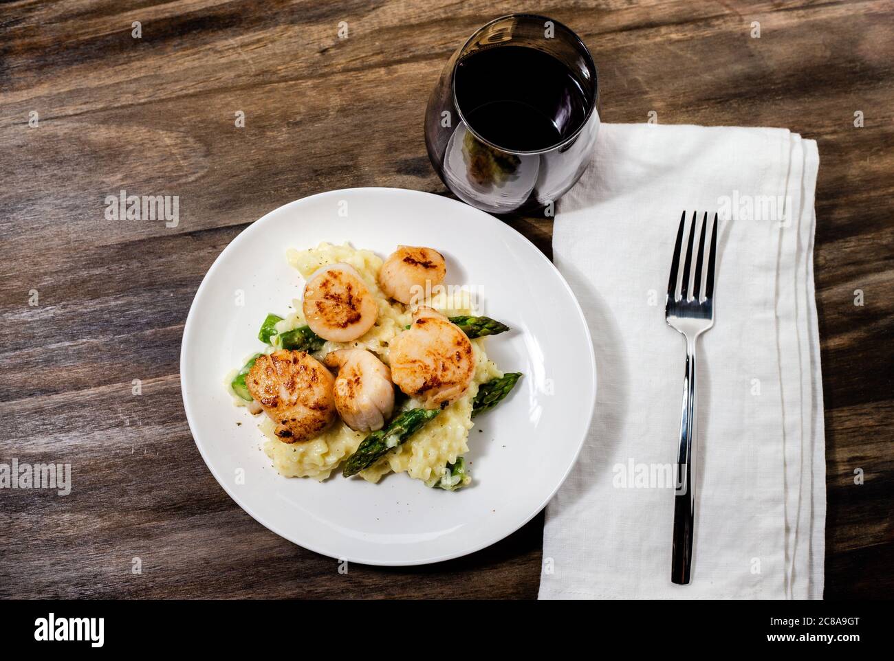 Gebratene Jakobsmuscheln über einem Spargelrisotto mit einem Glas Rotwein Stockfoto