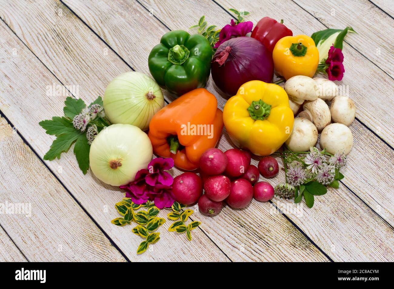 Frisches Bio geerntetes Gemüse und Blumen auf Holztisch in künstlerischer Anordnung angezeigt, um gesunde Mahlzeiten zu fördern Stockfoto
