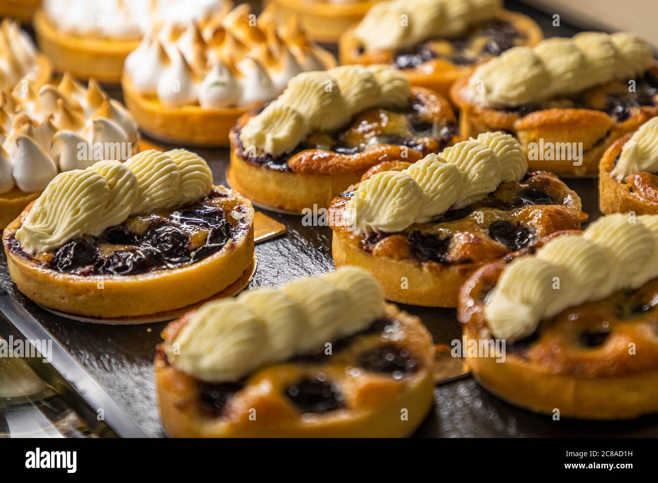 Mehrere Torten mit einer dunklen Beerenfüllung stehen in der Vitrine der Bäckerei Kult auf der Riehentorstrasse in Basel, Schweiz. Einige der Mürbeteigböden sind mit einem flambierten Baiserwirbel bedeckt, andere mit gezogener Sahne. Stockfoto