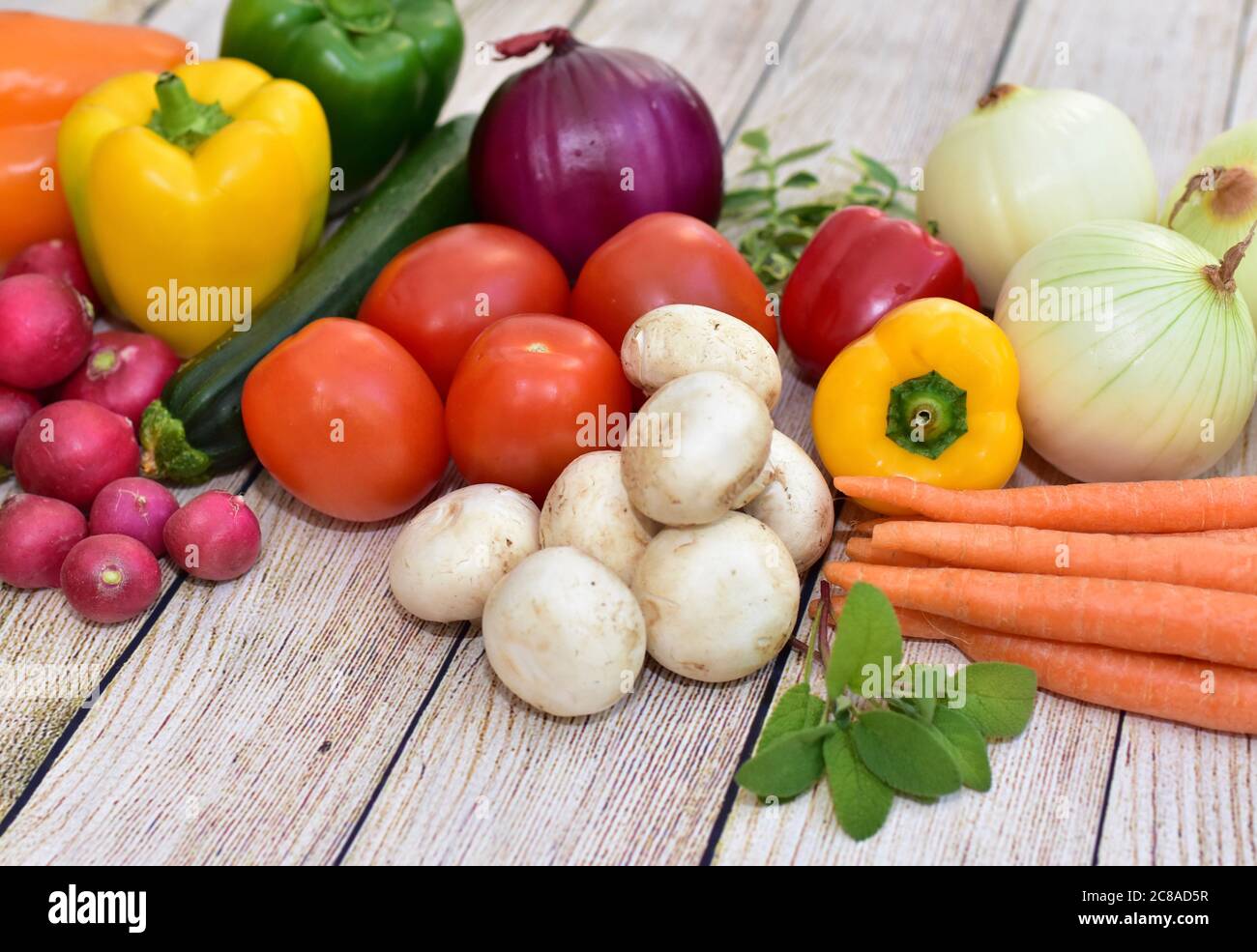 Frisches Bio geerntetes Gemüse und Blumen auf Holztisch in künstlerischer Anordnung angezeigt, um gesunde Mahlzeiten zu fördern Stockfoto