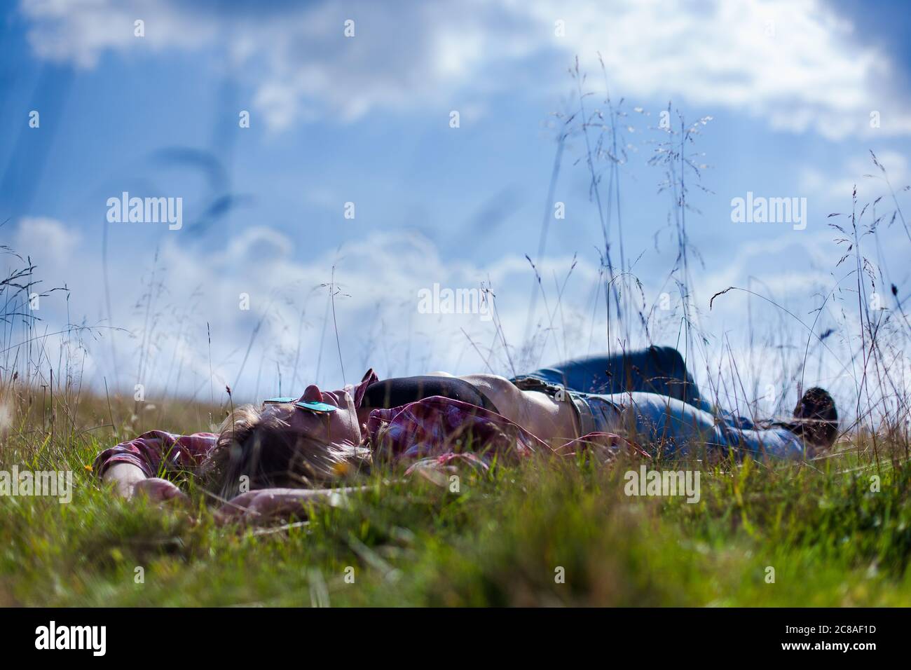 Nettes Mädchen in Denim Kleidung liegt auf dem Gras vor einem Hintergrund von Wolken Stockfoto