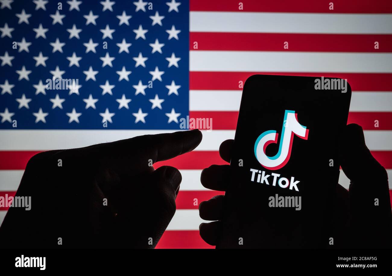 Stone / Großbritannien - Juli 22 2020: TikTok-Logo auf der Silhouette des Smartphones gesehen halten in der Hand mit verschwommener amerikanischer Flagge auf der Rückseite. Neu Stockfoto