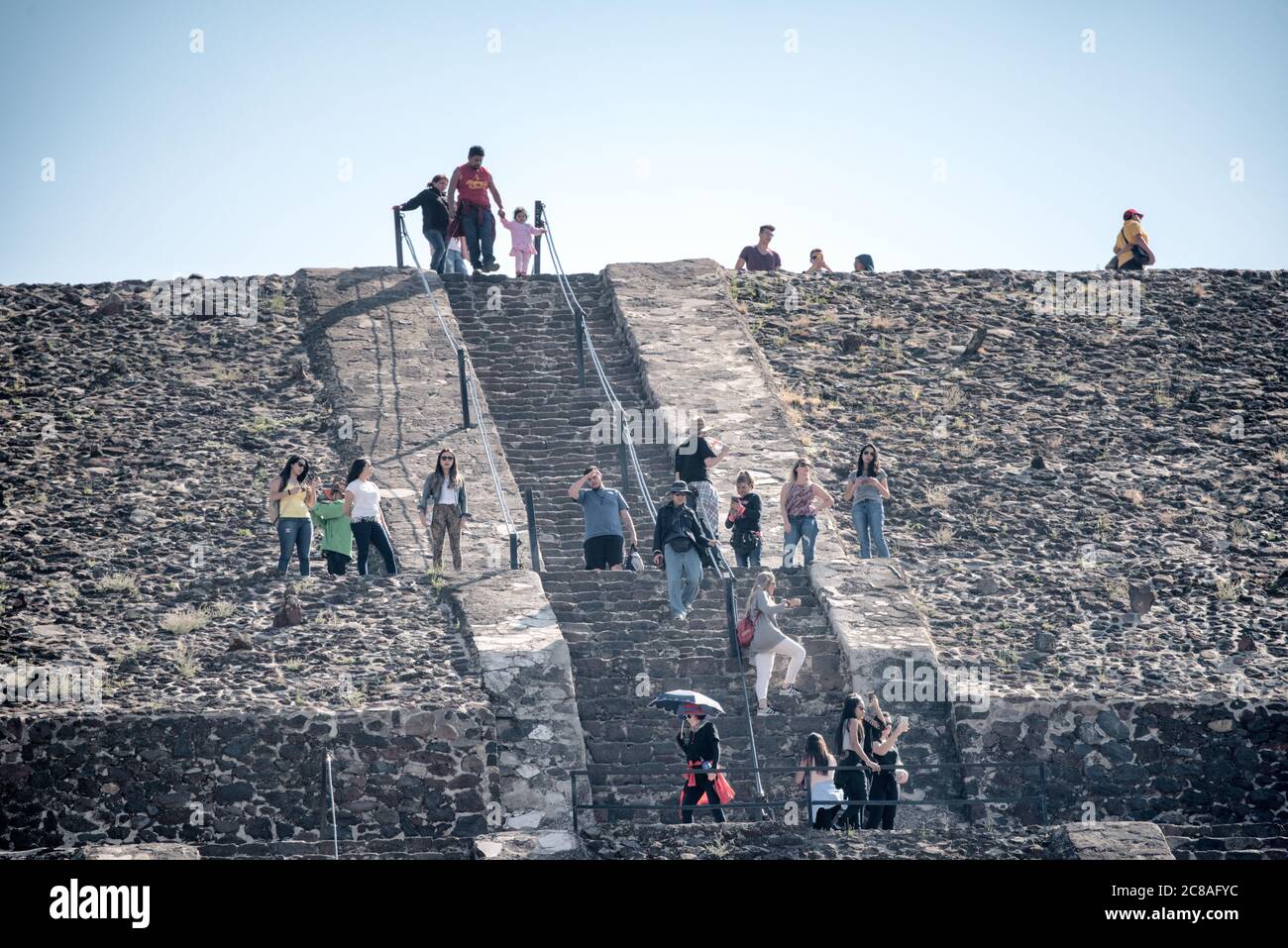 Pyramide der Sonne Besucher Teotihuacan Mexiko // TEOTIHUACAN, Mexiko — Besucher klettern die steilen Stufen der Pyramide der Sonne an der archäologischen Stätte Teotihuacan. Dieses monumentale Gebäude, eine der größten antiken Pyramiden Amerikas, erhebt sich etwa 216 Fuß (66 Meter) hoch und misst etwa 720 Fuß (220 Meter) an seiner Basis. Die Pyramide wurde um 100-450 n. Chr. von der antiken Teotihuacan-Zivilisation errichtet, deren Identität den Archäologen weitgehend unbekannt ist. Teotihuacan war eine der größten Städte in der Antike, mit einer Bevölkerung von bis zu zehn Stockfoto