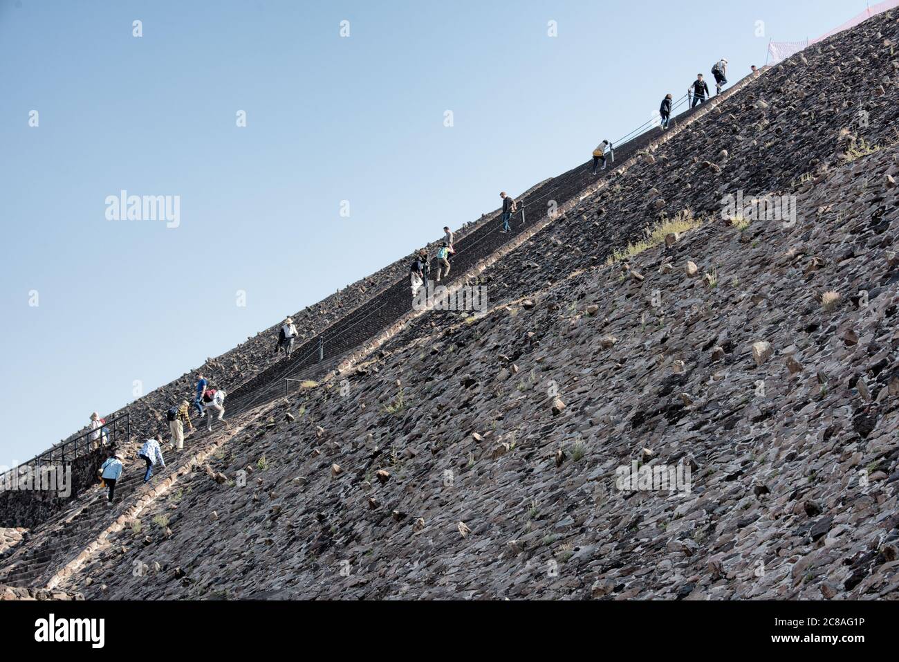 Pyramide der Sonne Besucher Teotihuacan Mexiko // TEOTIHUACAN, Mexiko — Besucher klettern die steilen Stufen der Pyramide der Sonne an der archäologischen Stätte Teotihuacan. Dieses monumentale Gebäude, eine der größten antiken Pyramiden Amerikas, erhebt sich etwa 216 Fuß (66 Meter) hoch und misst etwa 720 Fuß (220 Meter) an seiner Basis. Die Pyramide wurde um 100-450 n. Chr. von der antiken Teotihuacan-Zivilisation errichtet, deren Identität den Archäologen weitgehend unbekannt ist. Teotihuacan war eine der größten Städte in der Antike, mit einer Bevölkerung von bis zu zehn Stockfoto