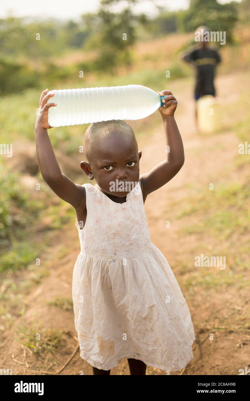 Ein junges Mädchen im Alter von 2 Jahren holt mit ihrem Bruder Wasser im ländlichen Rakai District, Uganda, Ostafrika. Stockfoto