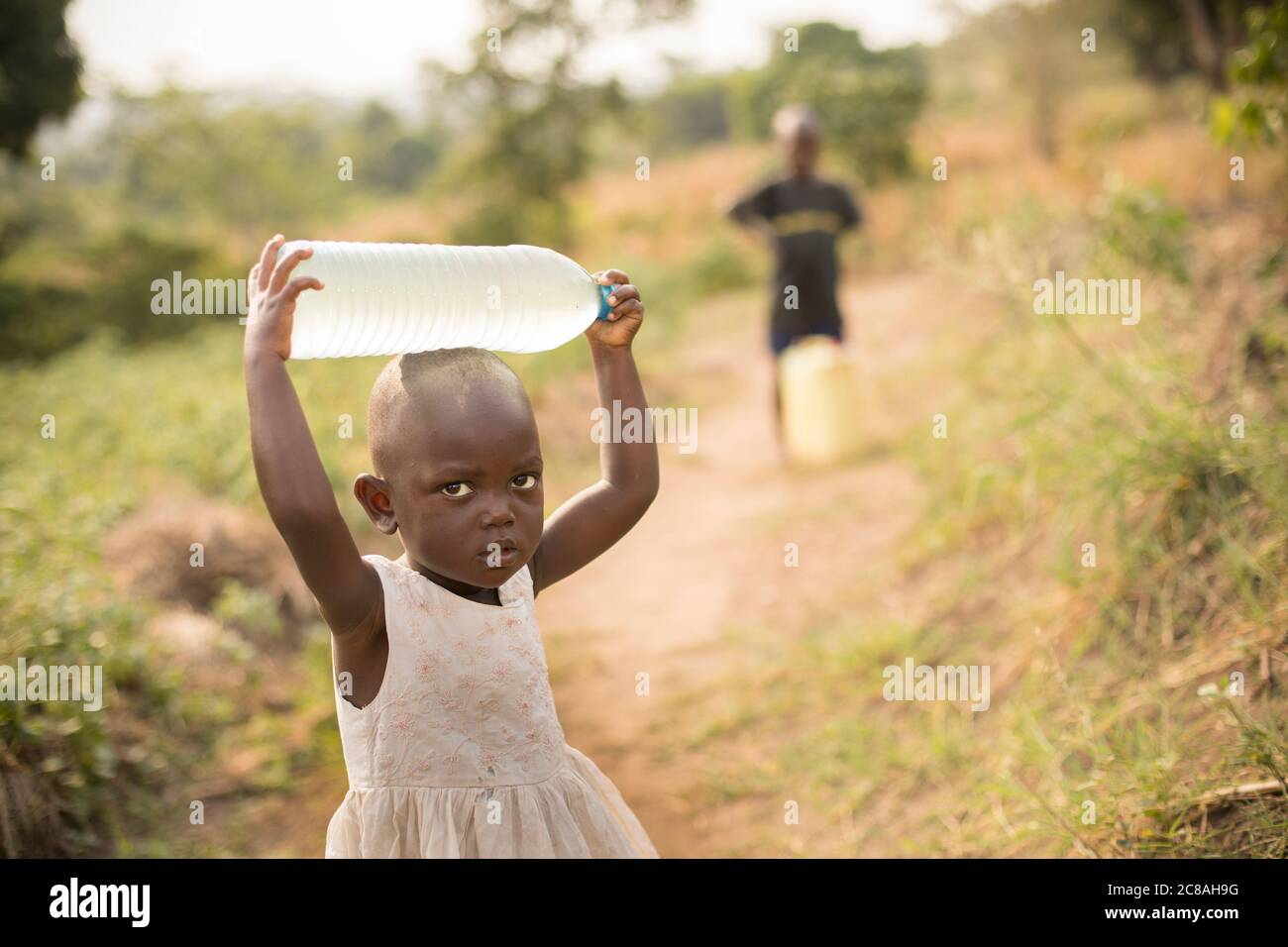 Ein junges Mädchen im Alter von 2 Jahren holt mit ihrem Bruder Wasser im ländlichen Rakai District, Uganda, Ostafrika. Stockfoto