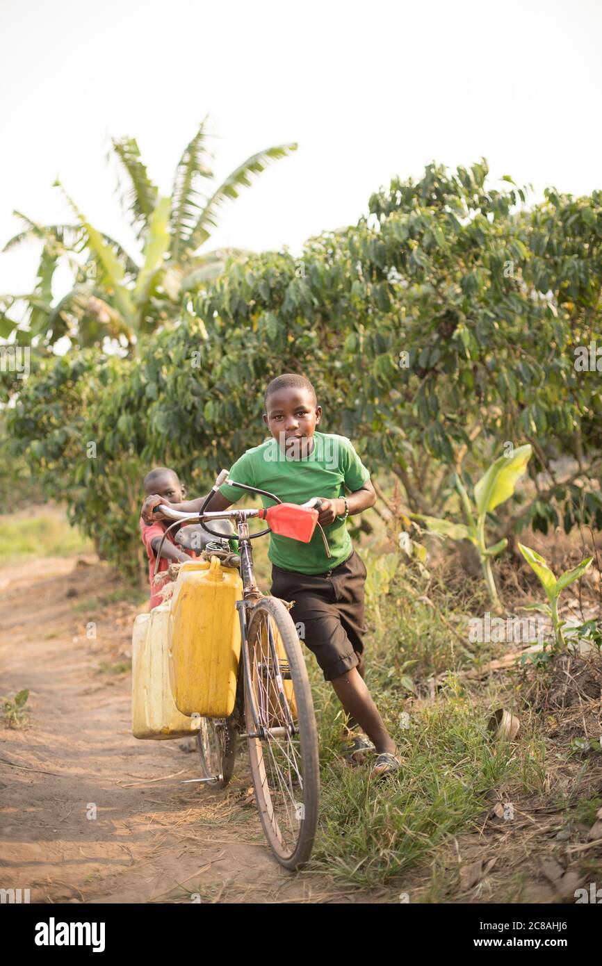 Kinder nutzen ein Fahrrad, um Wasser in einem ländlichen Dorf im Rakai District, Uganda, Ostafrika zu holen und zu transportieren. Stockfoto