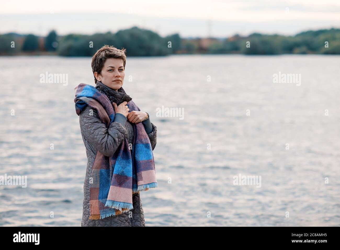 Frau in grauem Mantel und lila Schal am See, Stockfoto