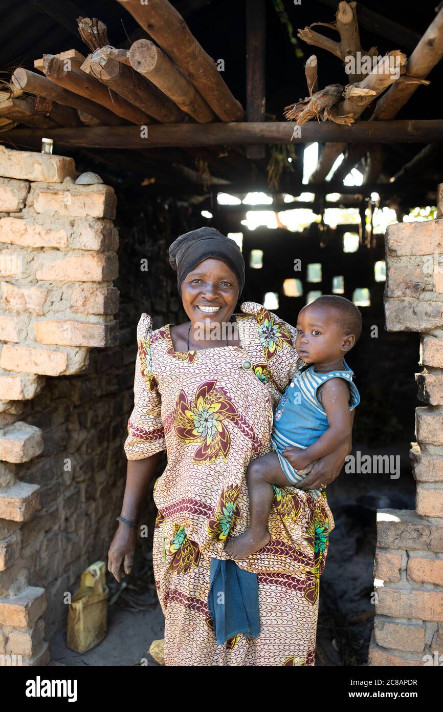 Porträt einer afrikanischen Mutter in einem traditionellen ugandischen Gomesi-Kleid, während sie ihr Kind in der Tür ihrer Hütte in Lyantondo, Uganda, hält. Stockfoto