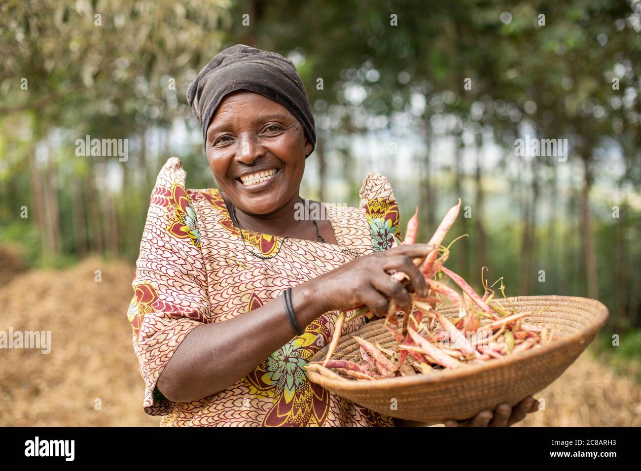 Eine lächelnde Bäuerin hält einen Korb ihrer frisch geernteten Bohnenernte auf ihrer Farm im ländlichen Lyantonde District, Uganda, Ostafrika. Stockfoto