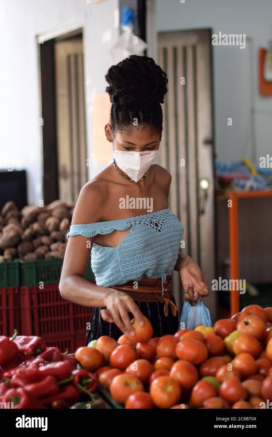 Junge schwarze lateinische Frau Kauf Gemüse in Gesichtsmaske Stockfoto