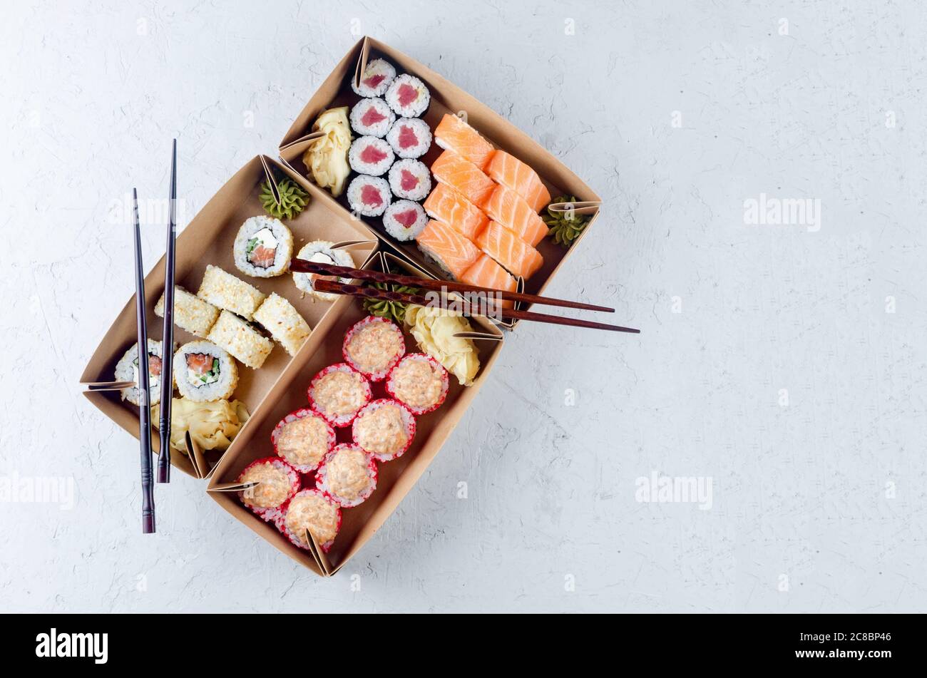 Leckere Sushi-Brötchen in Einweg-Kraftpapier-Boxen, Saucen, Essstäbchen. Sushi zum Mitnehmen oder Anliefern Stockfoto