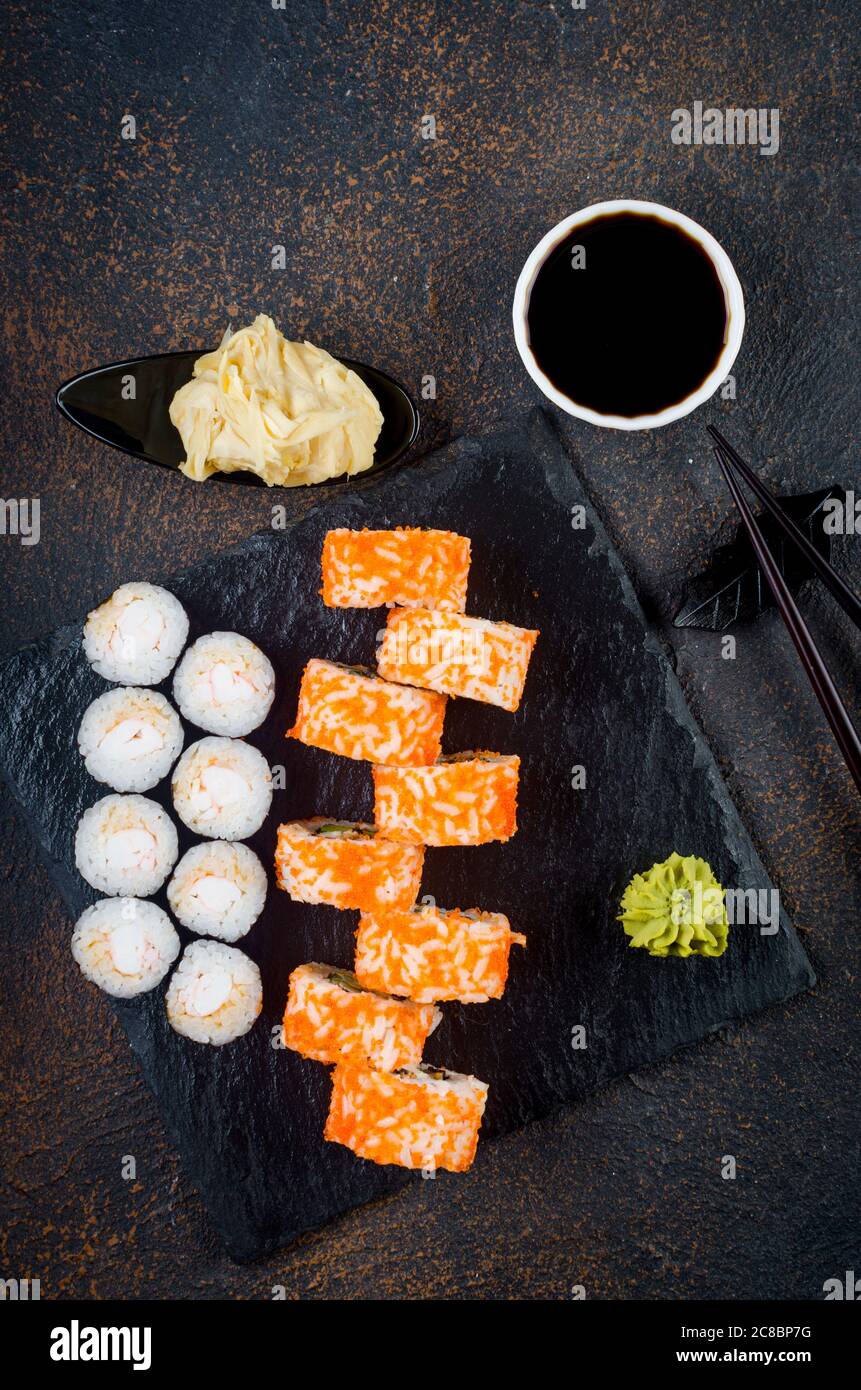 Maki-Brötchen auf Steinplatte mit Soßen, Ingwer und Wasabi Stockfoto