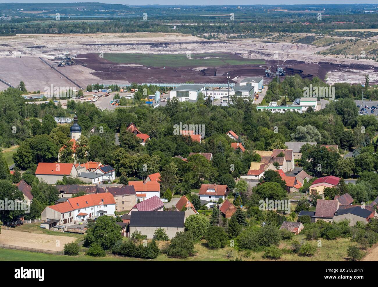 13. Juli 2020, Sachsen, Pödelwitz: Das Dorf liegt nur 500 Meter vom Vereinigten Schlenhain Tagebau entfernt. Das Dorf im Leipziger Braunkohlebergbaugebiet will ein Vorzeigeprojekt des Strukturwandels werden. Pödelwitz sollte eigentlich ausgebaggert werden, sieht sich aber nach dem Kohleausstieg gerettet. Ein großer Teil der Einwohner hat das Dorf vor Jahren verlassen, nur acht von 40 Parzellen sind noch bewohnt. (Luftaufnahme mit Drohne) Foto: Jan Woitas/dpa-Zentralbild/ZB Stockfoto