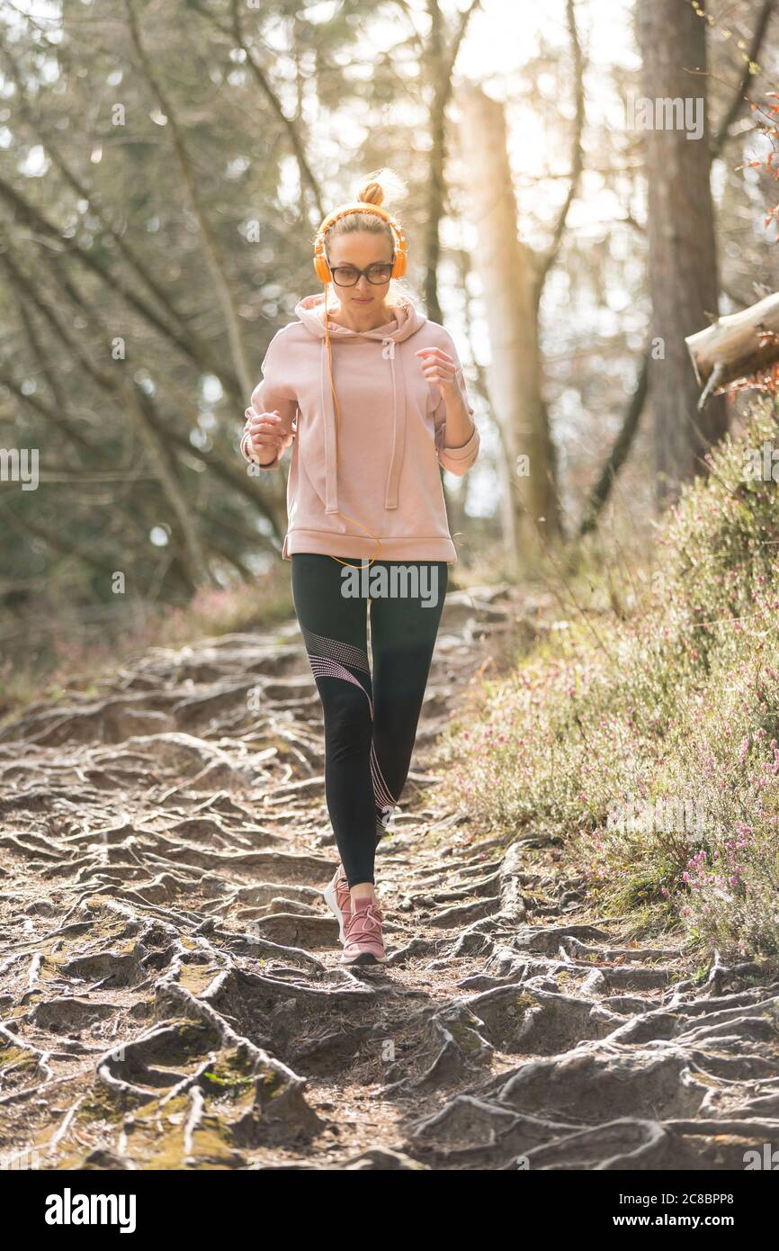 Aktive sportliche Frau, die während des Laufs im Herbstwald Musik hört. Laufbeine trainieren im Freien. Gesundes Lebensgefühl junger Menschen Stockfoto