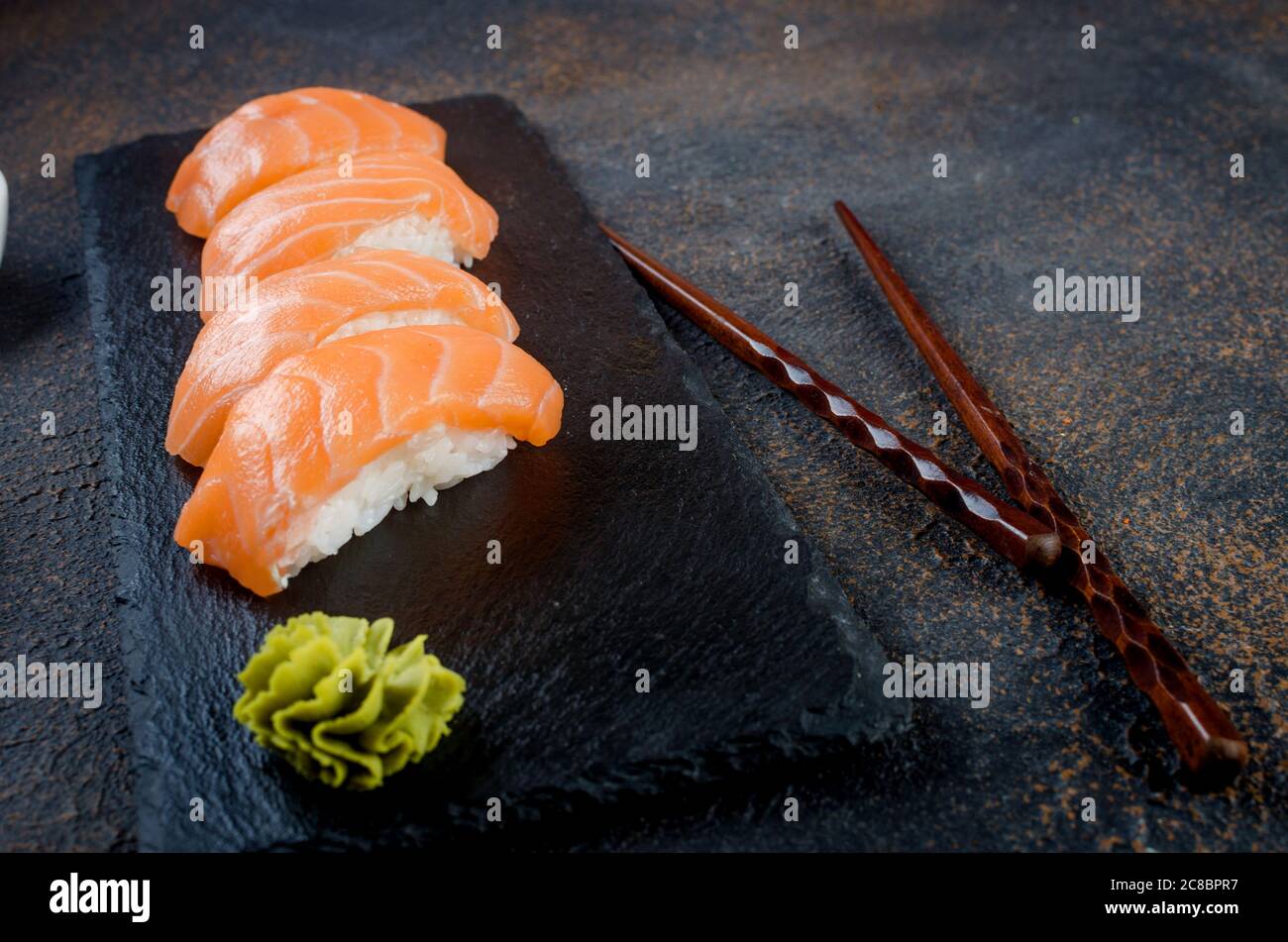 Leckeres Nigiri Sushi mit Lachs auf schwarzem Steinteller mit Sojasoße, Ingwer, Wasabi Stockfoto