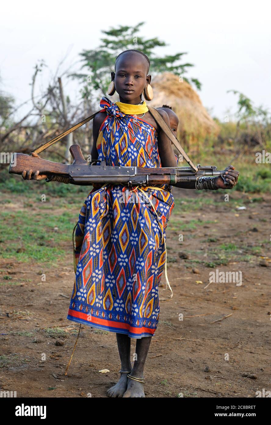 Äthiopien - Afrika, Januar 03. 2014: Mädchen von Mursi Stamm mit Kind und Maschinengewehr, Mago Nationalpark, Äthiopien, Afrika Stockfoto