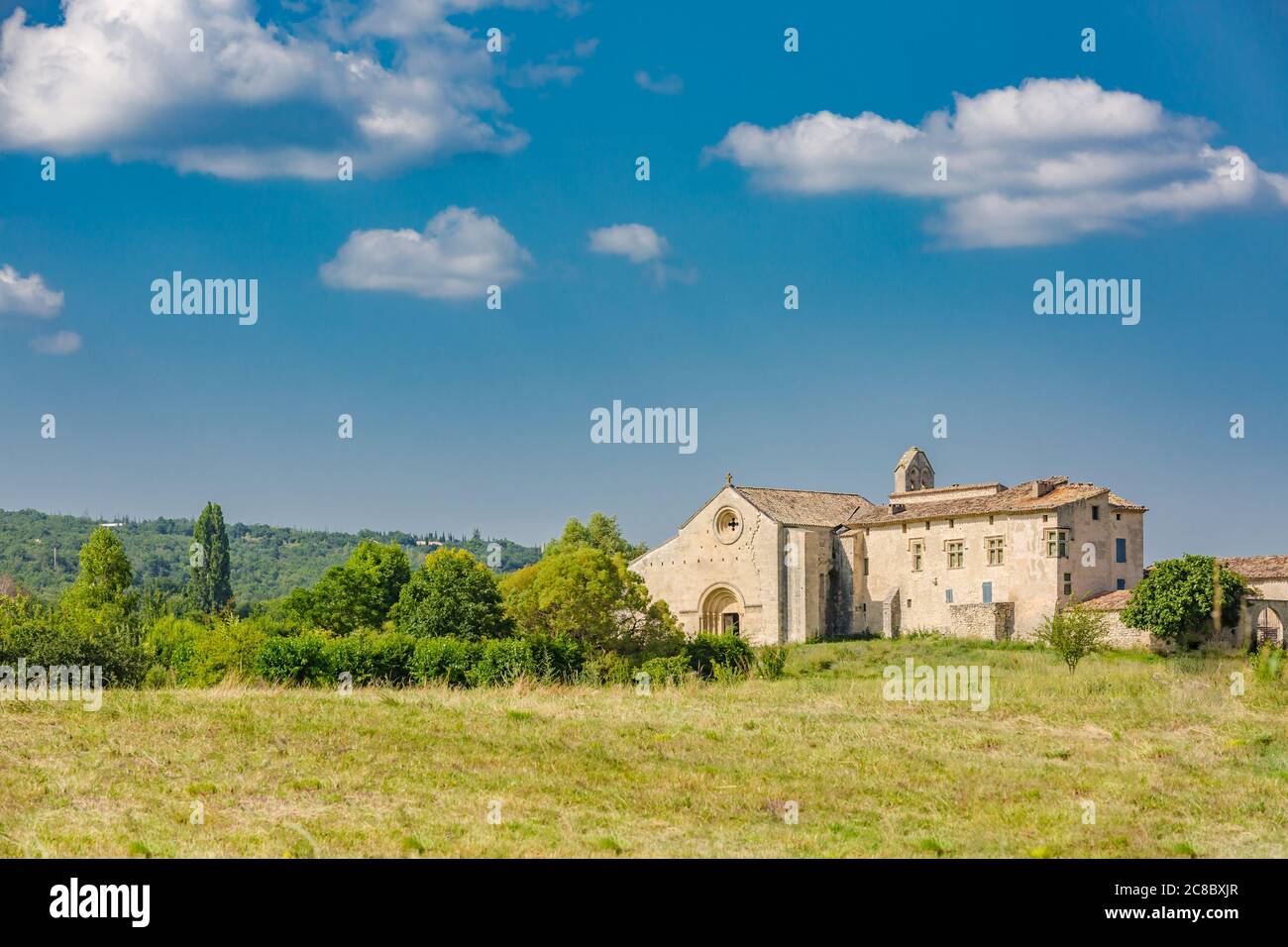 Bilderhaftes Steinmonasterium neben grüner Wiese im sommerlichen Provence-Land. Malerische ländliche Landschaft Frankreich. Friedlicher Reise-Wanderlust-Natur Stockfoto