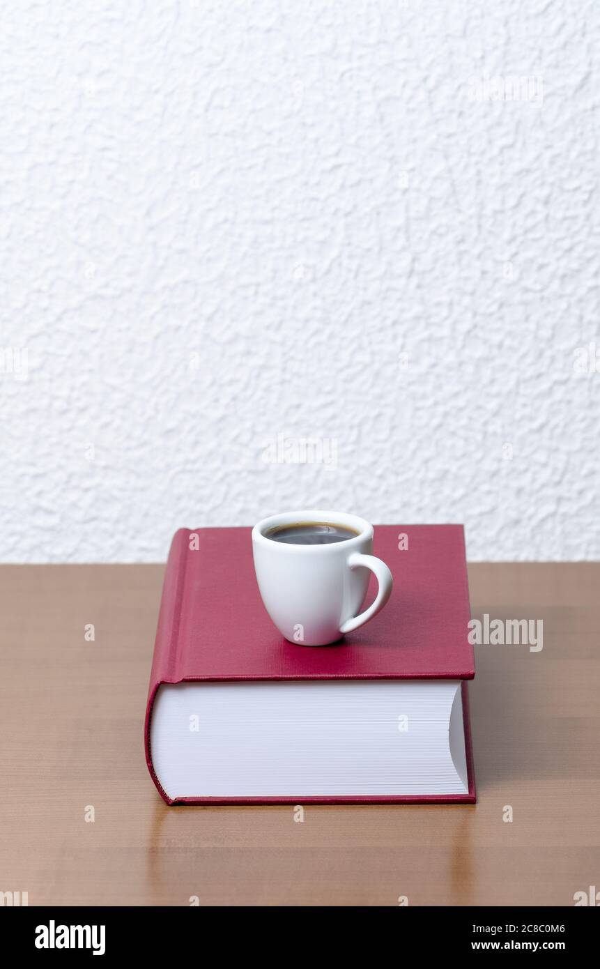 Rote Hardcover-Bücher und weiße Kaffeetasse oder Tasse mit heißem Getränk auf Holztisch oder Schreibtisch gegen weiße Wand, innen, Literatur, Bibliothek Stockfoto