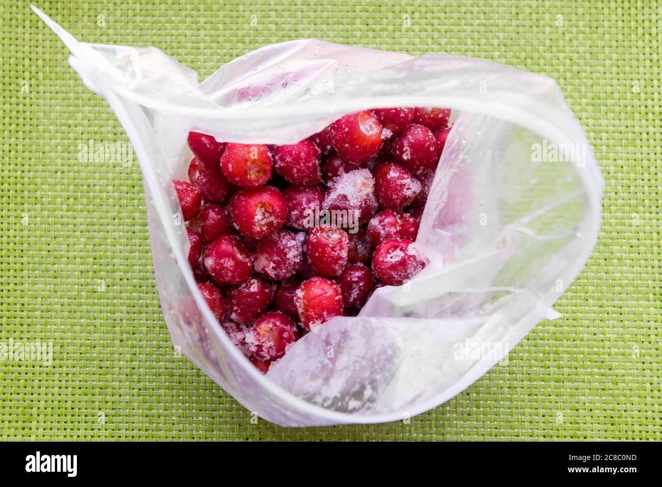 Gefrorene Kirschen in einer offenen Plastiktüte von leicht oben auf grüner Tischdecke Stockfoto