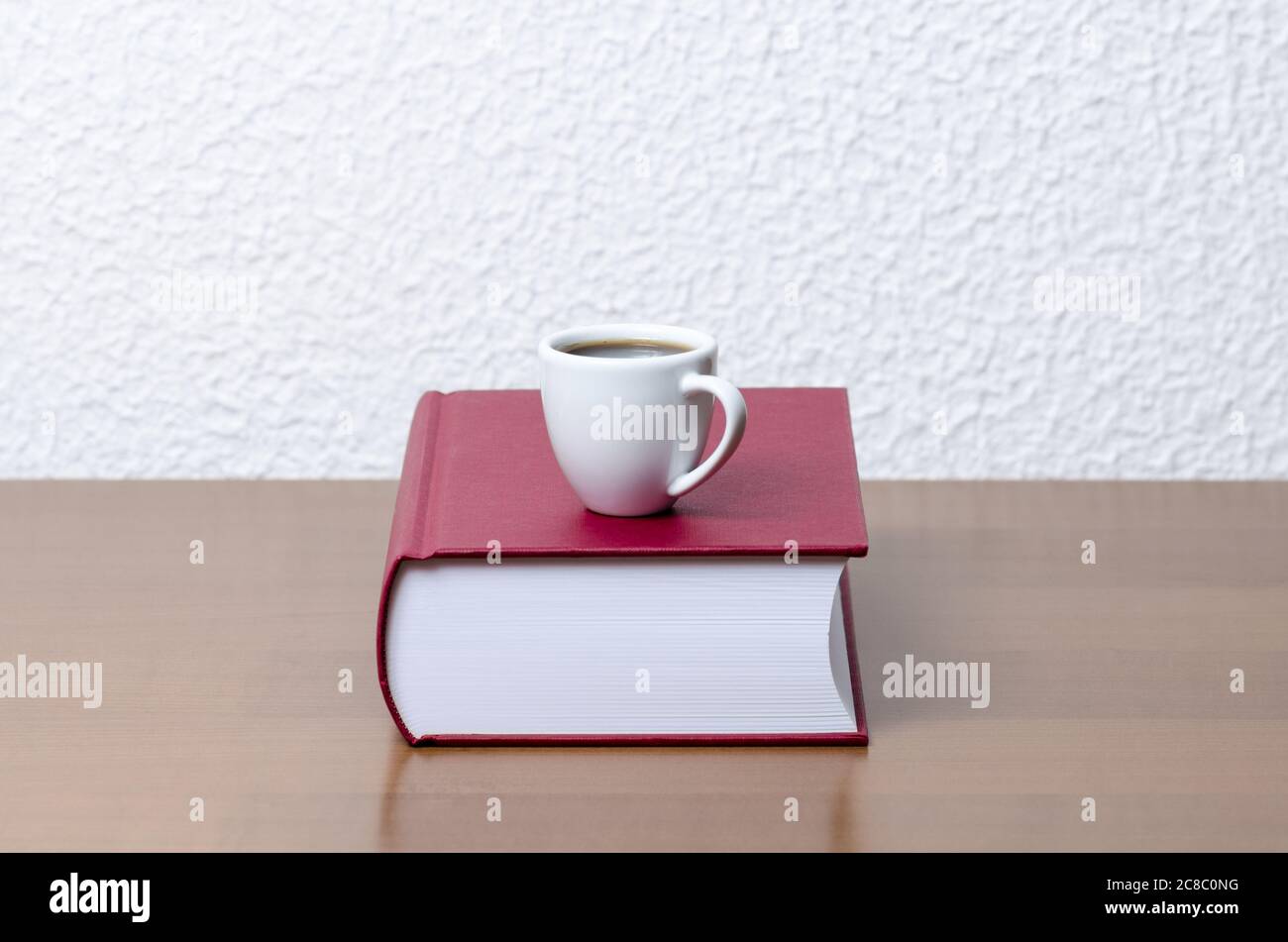 Rote Hardcover-Bücher und weiße Kaffeetasse oder Tasse mit heißem Getränk auf Holztisch oder Schreibtisch gegen weiße Wand, innen, Literatur, Bibliothek Stockfoto