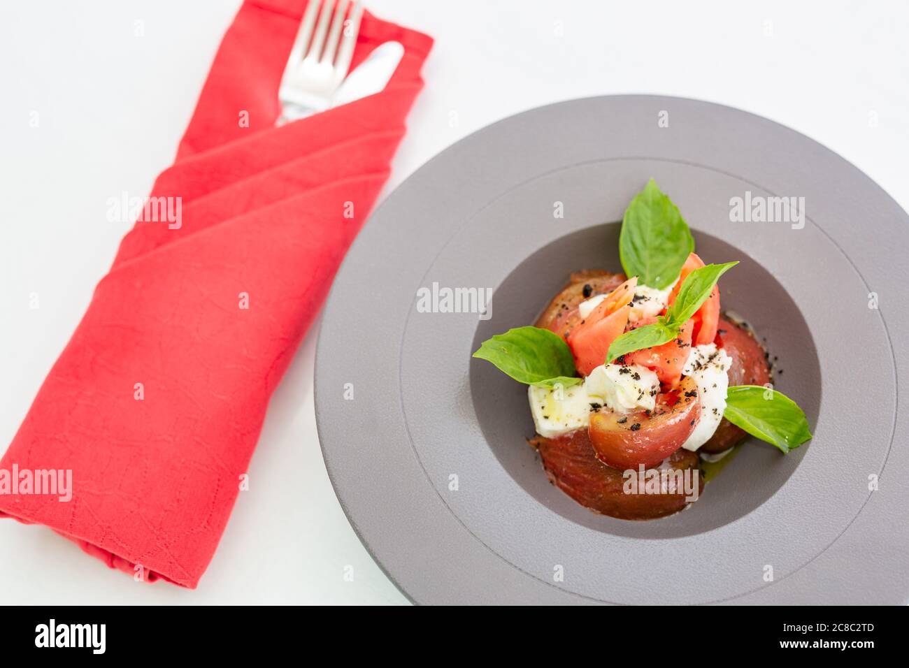 Luxussalat isoliert auf weiß mit Besteck und roter Serviette. Gourmet-Tomaten und Mozzarella-Salat Stockfoto