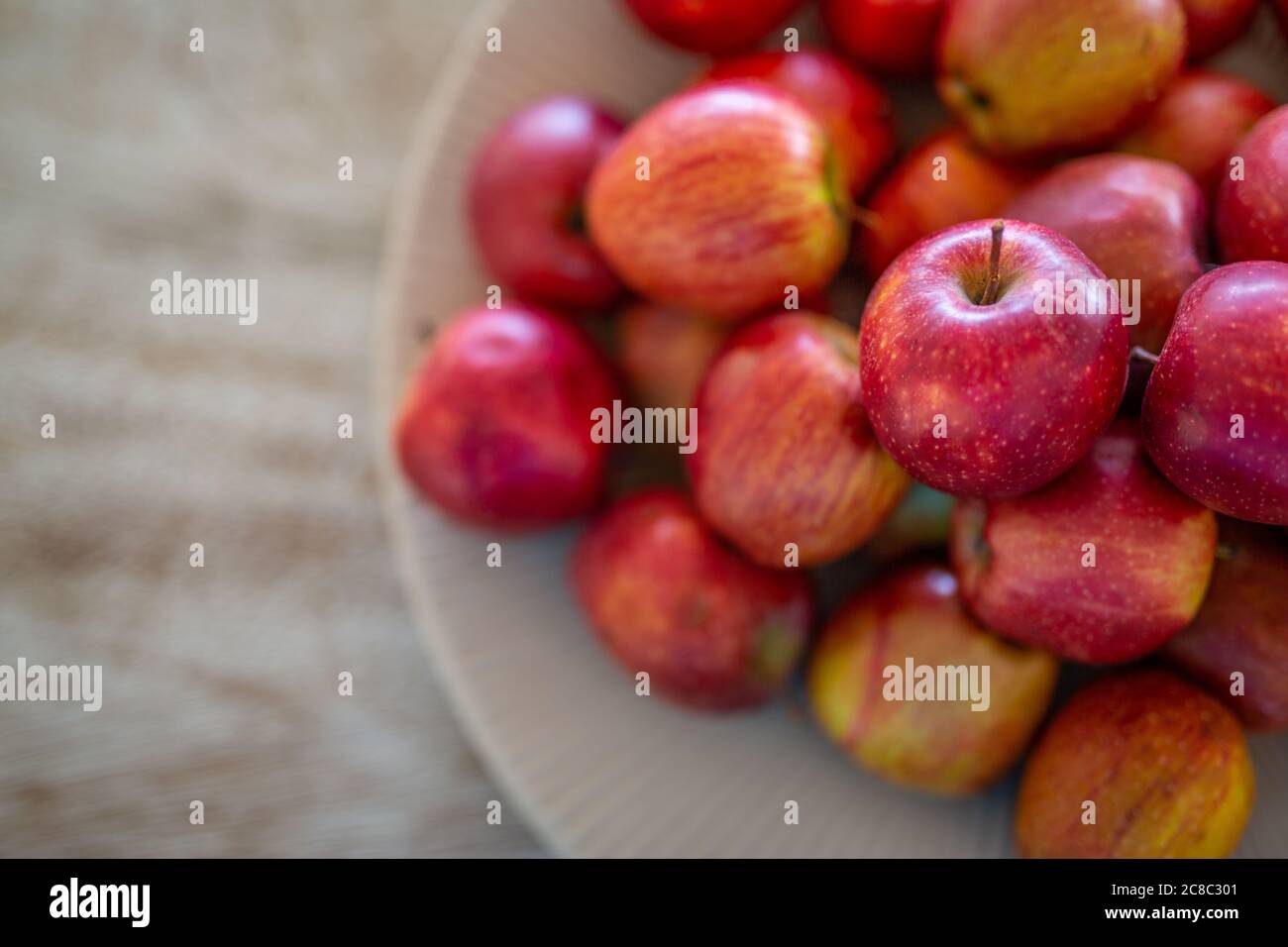 Frische rote Äpfel in einer weißen Schale über Holztischplatte, weiches künstlerisches Licht Stockfoto