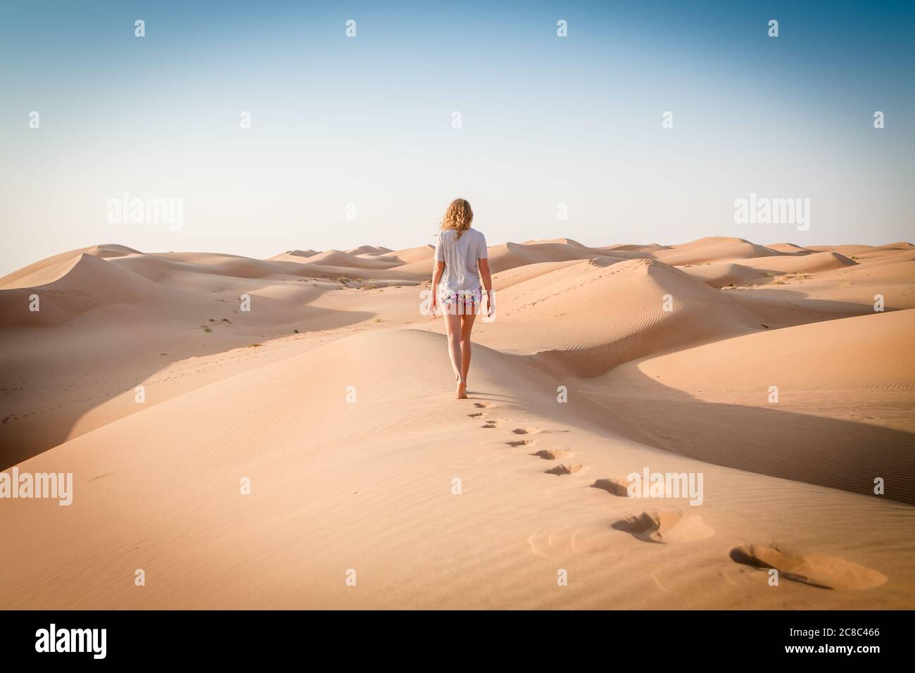 Blonde weibliche kaukasische Reisende verlassen Fußspuren in Sanddünen, wenn in Dessert in Oman zu Fuß Stockfoto