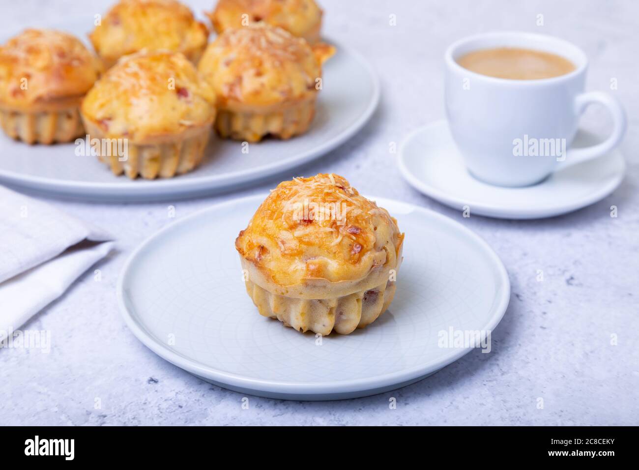 Muffins mit Schinken und Käse. Hausgemachtes Backen. Im Hintergrund ist ein Teller mit Muffins und eine Tasse Kaffee. Nahaufnahme. Stockfoto