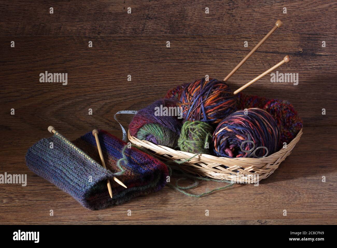 Stricken und Wolle in einem Korb auf Holzoberfläche Stockfoto
