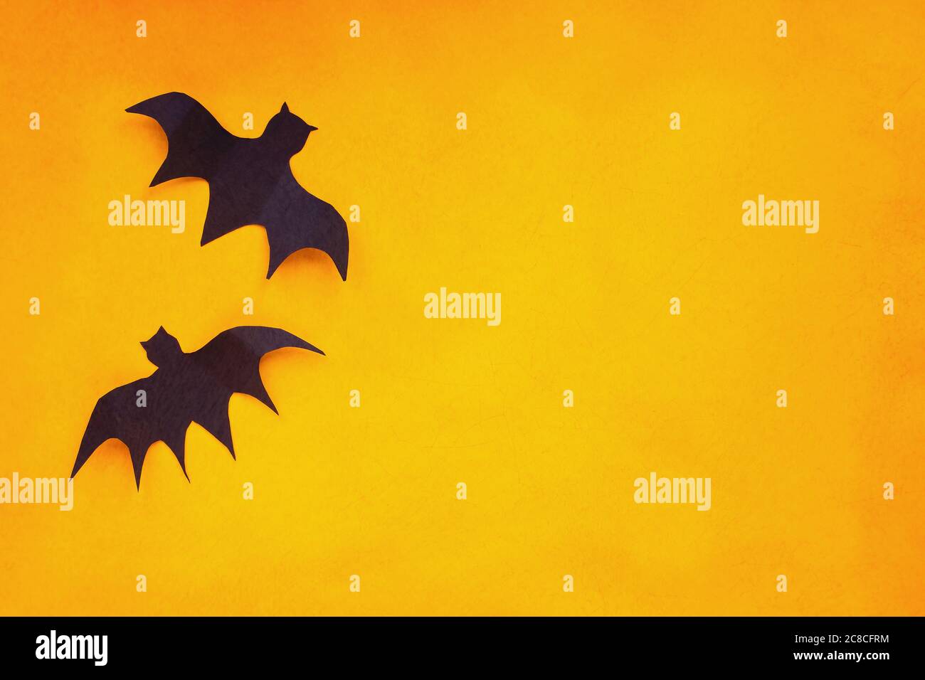 Halloween Feiertagsdekorationen von zwei Papierfledermäusen fliegen über einen leeren orangen Hintergrund mit freiem Platz für Text. Stockfoto